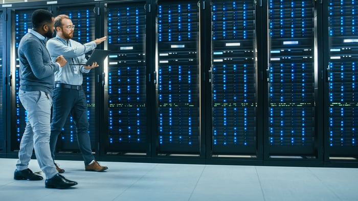 Two people talking while walking past servers inside a data center.